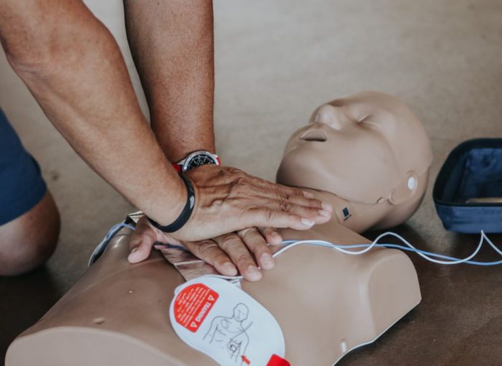 pexels-photo-11655091-11655091 Hands demonstrating CPR technique on a training mannequin with AED.